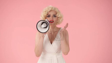 Photo for Woman in character of Marilyn Monroe speaking into megaphone. Woman with colorful makeup, wig and white dress in studio on pink background. Sale, Black Friday. Copy space - Royalty Free Image