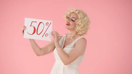 Foto de Mujer sosteniendo un cartel que dice el cincuenta por ciento. Mujer parecida a Marilyn Monroe en el estudio sobre fondo rosa. Venta, viernes negro, descuentos - Imagen libre de derechos