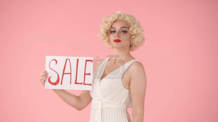 Foto de Mujer sosteniendo un cartel con la etiqueta Sale. Mujer en la mirada de Marilyn Monroe en el estudio sobre fondo rosa de cerca. Venta, viernes negro, descuentos - Imagen libre de derechos