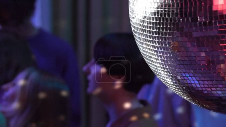 Téléchargez les photos : Gros plan capturant une balle disco éclatante. Photo floue d'un groupe d'adolescents dansant dans une pièce décorée en arrière-plan. Néon lumières colorées. Vie nocturne, publicité ou contenu créatif. - en image libre de droit
