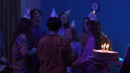 Foto de Grupo de adolescentes que celebran el cumpleaños de las niñas en una sala de fiestas decorada, borrosa en el fondo. Alguien está trayendo un pastel con velas encendidas. Luces de colores neón. Anuncio o creativo - Imagen libre de derechos