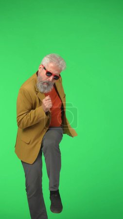 Foto de Concepto de personas mayores modernas creativas. Retrato de hipster con estilo senior en Chroma pantalla verde clave de fondo, el hombre bailando se ve genial en la cámara. Área de publicidad, maqueta de espacio de trabajo. Foto vertical. - Imagen libre de derechos