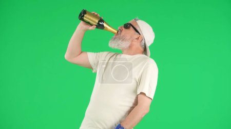 Foto de Concepto de personas mayores modernas creativas. Retrato de hombre mayor hipster en Chroma pantalla verde clave de fondo, hombre en camiseta blanca beber champán de la botella. Área de publicidad, maqueta del espacio de trabajo. - Imagen libre de derechos