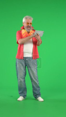 Photo for Creative modern seniors concept. Portrait of senior hipster on Chroma key green screen background, man watching funny videos online on tablet. Advertising area, workspace mockup. Vertical photo. - Royalty Free Image