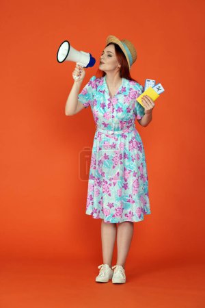 Photo for Travelling and vacation advertisement concept. Studio shot of female model. Woman standing holding flight tickets, passport and saying advertising in small megaphone, isolated on orange background. - Royalty Free Image
