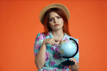 Photo for Travelling advertisement concept. Studio shot of female model. Close up of woman looking at the camera holding globe, pointing at the map with upset face expression, isolated on orange background. - Royalty Free Image