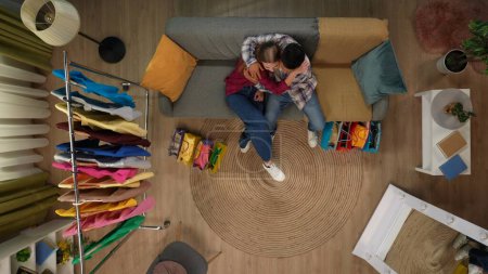 Photo for Shopping, leisure and lifestyle advertisement concept. Top view of modern apartment living room. Shot of man and woman sitting on the couch hugging happy after shopping, many gift bags around. - Royalty Free Image