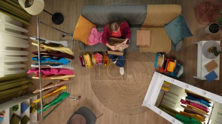 Photo for Shopping, leisure and lifestyle advertisement concept. Top view of modern apartment living room. Girl sitting on the sofa opens cardboard box and looks at the package she received, positive expression - Royalty Free Image