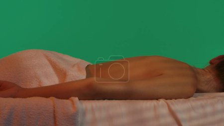 Téléchargez les photos : Bien-être du corps concept créatif. Salon de spa, cliente posée sur une table de massage couverte d'une serviette blanche, ambiance relaxante. Clé chroma fond d'écran vert, espace de publicité maquette espace de travail. - en image libre de droit