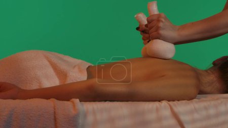 Photo for Body wellbeing creative concept. Spa salon, female on massage table, woman massaging clients back with hot herb compress bags. Chroma key green screen background, advertising area workspace mockup. - Royalty Free Image