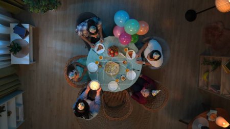 Photo for Family bonding and relationships concept. Scene in the apartment room. Top view of table with party food and drinks. Family with friends celebrating little girl birthday, mom brings cake with candles. - Royalty Free Image