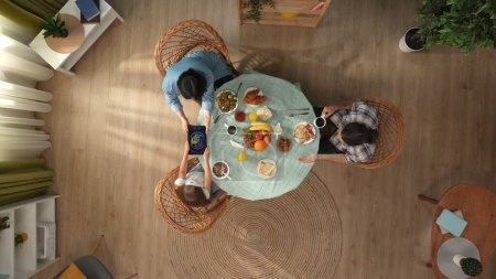 Photo for Family bonding and relationships concept. Scene in the apartment room. Top view of family sitting at the table eating breakfast, mother tries to take away tablet with video from daughter. - Royalty Free Image