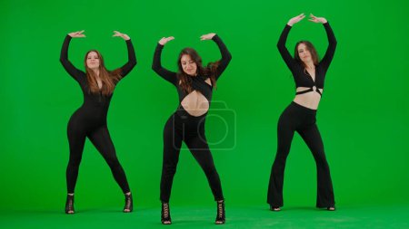 Téléchargez les photos : Groupe de femmes dansant talons dansent sur écran vert chroma fond clé dans un studio. Costume sexy noir, talons hauts. Chorégraphie sensuelle moderne. Sur toute la longueur. Clip promotionnel ou publicité. - en image libre de droit