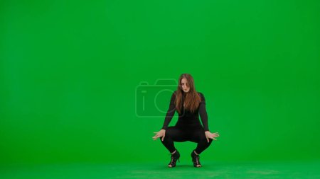 Téléchargez les photos : Jolies femmes dansant talons dansent sur fond de chroma écran vert clé dans un studio. Costume sexy noir, talons hauts. Chorégraphie sensuelle moderne. Sur toute la longueur. Clip promotionnel ou publicité. - en image libre de droit