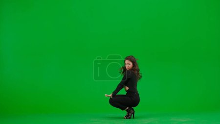 Photo for Attractive woman dancing heels dance on green screen chroma key background in a studio. Black sexy costume, high heels. Modern sensual choreography. Full length. Promotional clip or advertisement. - Royalty Free Image