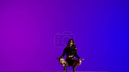 Photo for Attractive woman dancing heels dance in a studio. Blue to purple neon gradient background, striped falling shadow. Black sexy costume, high heels. Full length. Promotional clip or advertisement. - Royalty Free Image