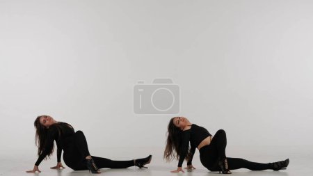 Téléchargez les photos : Deux femmes dansant talons dansent dans un studio. Fond blanc uni isolé. Costume sexy noir, talons hauts. Chorégraphie sensuelle moderne. Sur toute la longueur. Clip promotionnel ou publicité. - en image libre de droit