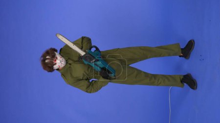 Photo for Man in white mask with chainsaw in hands on blue background. Image of maniac Jason Voorhees from Friday 13. Full length. Halloween celebration concept. - Royalty Free Image