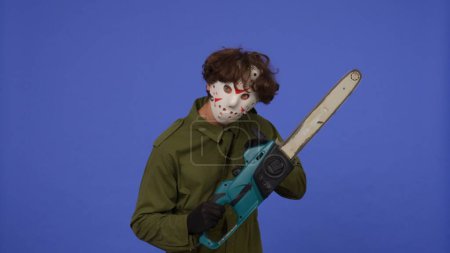 Photo for Man in white mask with chainsaw in hands on blue background. Image of maniac Jason Voorhees from Friday 13. Halloween celebration concept. - Royalty Free Image