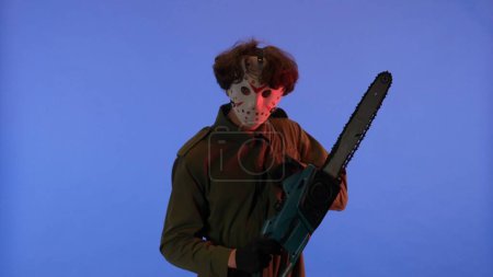 Photo for Man in white mask with chainsaw in hands on blue background with red neon light. Image of maniac Jason Voorhees from Friday 13. Halloween celebration concept. - Royalty Free Image