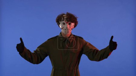 Photo for Man in white mask showing finger up gesture on blue background with red neon light. Image of maniac Jason Voorhees from Friday 13. Workspace, advertisement. Halloween celebration concept. - Royalty Free Image