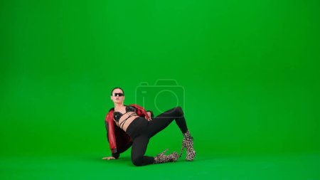 Photo for Modern dance style creative advertisement concept. Attractive woman dancer on the floor posing in high heels on chroma key green screen background in a studio. Advertising area, workspace mockup. - Royalty Free Image