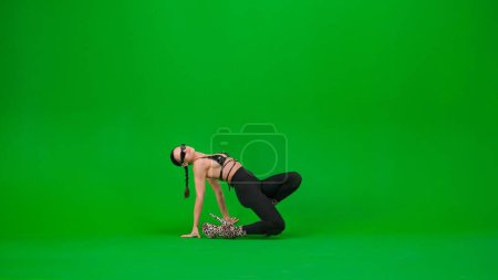 Téléchargez les photos : Style de danse moderne concept publicitaire créatif. Danseuse attirante sur le sol en talons hauts montre élément sur fond de studio écran vert chroma clé. Espace publicitaire, maquette de l'espace de travail. - en image libre de droit