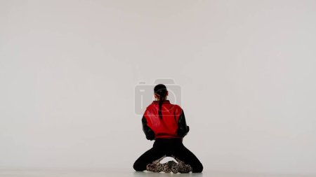 Foto de Concepto de publicidad creativa estilo danza moderna. Retrato de bailarina. Mujer atractiva bailarina con chaqueta y tacones altos sentada en el suelo en el estudio. Aislado sobre fondo blanco. - Imagen libre de derechos