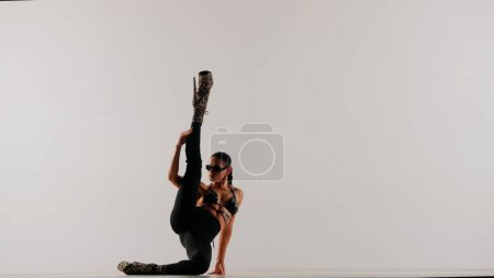 Téléchargez les photos : Style de danse moderne concept publicitaire créatif. Portrait de danseuse. Danseuse séduisante portant des talons hauts allongés sur le sol tenant la jambe vers le haut dans le studio. Isolé sur fond blanc. - en image libre de droit