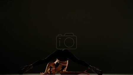 Photo for Modern dance style creative advertisement concept. Portrait of female dancer. Appealing woman dancer in high heels standing with legs split up at the camera in studio. Isolated on black background. - Royalty Free Image