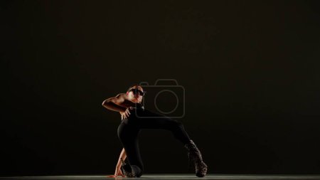 Téléchargez les photos : Style de danse moderne concept publicitaire créatif. Portrait de danseuse. Danseuse séduisante en talons hauts posant à genoux devant la caméra en studio. Isolé sur fond noir. - en image libre de droit