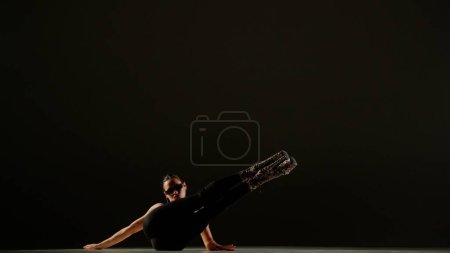 Téléchargez les photos : Style de danse moderne concept publicitaire créatif. Portrait de danseuse. Danseuse séduisante en talons hauts allongés sur le sol avec les jambes vers le haut à la caméra en studio. Isolé sur fond noir. - en image libre de droit