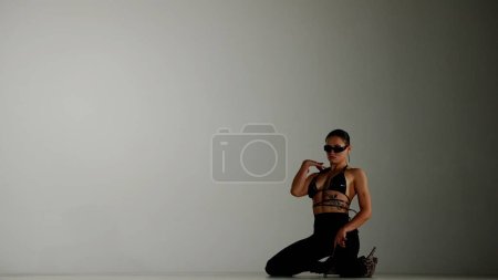 Téléchargez les photos : Style de danse moderne concept publicitaire créatif. Portrait de danseuse. Femme danseuse en talons hauts assise sur le sol dans le studio regardant la caméra. Isolé sur fond de dégradé blanc - en image libre de droit