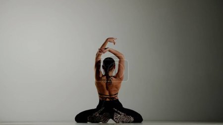 Foto de Concepto de publicidad creativa estilo danza moderna. Retrato de bailarina. Bailarina con tacones altos sentada en el suelo posando con la espalda en el estudio. Aislado sobre fondo de degradado blanco - Imagen libre de derechos