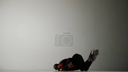 Photo for Modern dance style creative advertisement concept. Portrait of female dancer. Woman dancer in high heels laying on the floor, holding heels up in the studio. Isolated on white gradient background. - Royalty Free Image
