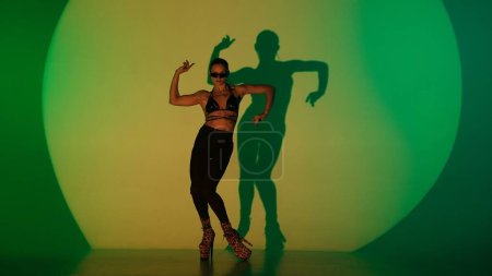 Photo for Modern dance style creative advertisement concept. Portrait of female dancer. Woman dancer in high heels shows choreography element in green yellow neon spotlight. Isolated on colorful background. - Royalty Free Image