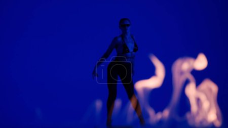 Téléchargez les photos : Style de danse moderne concept publicitaire créatif. Portrait de danseuse. Silhouette de danseuse séduisante en talons hauts posant en regardant la caméra, fond bleu dans le studio derrière les flammes. - en image libre de droit