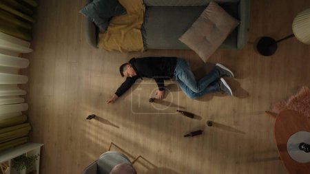 Téléchargez les photos : Vue de dessus d'un homme couché sur le sol à côté de bouteilles de bière vides. Alcoolisme. Désespoir. Traitement de la dépendance à l'alcool - en image libre de droit