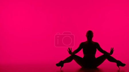 Photo for On pink background. Woman in silhouette wearing open clothes and high heels. Demonstrates a dance movement, pose. She is sitting on the floor with her legs slightly apart, she is sexy, plastic. - Royalty Free Image