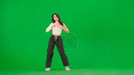 Foto de Coreografía de danza moderna concepto de publicidad creativa. Mujer atractiva en top blanco y pantalones negros de pie en pose de jazz funk danza en croma pantalla verde de fondo en un estudio. - Imagen libre de derechos