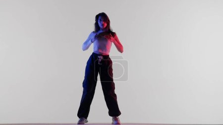 Photo for Modern dance choreography creative advertisement concept. Appealing woman in white top black pants and in red and blue neon light dancing jazz funk, isolated on white background in a studio. - Royalty Free Image