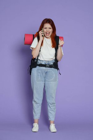 Photo for Tourism and active free time advertisement concept. Portrait of girl traveler. Woman tourist in casual with backpack talking on smartphone and shouting screaming in it . Isolated on purple background. - Royalty Free Image