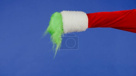 Photo for Green hairy Grinch hand showing thumbs down gesture on isolated blue background. Gift snatcher cosplay. Christmas and New Year celebration concept. Blue screen, chroma key - Royalty Free Image
