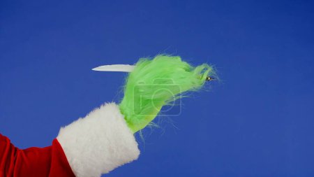 Foto de La mano de pelo verde Grinchs sostiene una pluma estilográfica. Cosplay secuestrador de regalos. Concepto de celebración de Navidad y Año Nuevo. Pantalla azul, croma key - Imagen libre de derechos