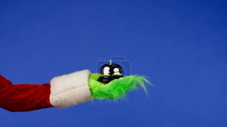 Foto de Grinchs mano de pelo verde sostiene la campana de recepción sobre un fondo azul aislado. Cosplay secuestrador de regalos. Concepto de celebración de Navidad y Año Nuevo. Pantalla azul, croma key - Imagen libre de derechos
