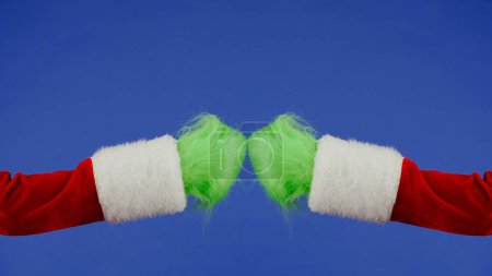 Téléchargez les photos : Grinches vertes mains poilues touchant les poings sur fond bleu isolé. Un cosplay de voleur de cadeaux. Noël et le concept de célébration du Nouvel An. Écran bleu, clé chromatique - en image libre de droit
