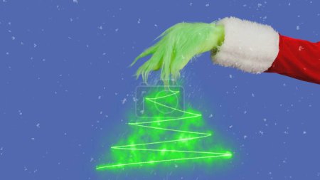Photo for Green hairy Grinch hand and Christmas tree graphic on isolated blue background. A place for your advertisement. Gift snatcher cosplay. New Year celebration concept. Blue screen, chroma key - Royalty Free Image