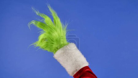 Téléchargez les photos : Main Grinch poilue verte montrant un geste OK sur fond bleu isolé. Un cosplay de voleur de cadeaux. Noël et le concept de célébration du Nouvel An. Écran bleu, clé chromatique - en image libre de droit
