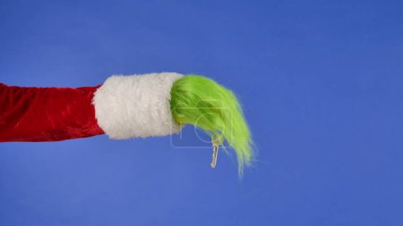 Foto de Manos peludas verdes del Grinch sosteniendo una llave de metal sobre un fondo azul aislado. Cosplay ladrón de regalos. Concepto de celebración de Navidad y Año Nuevo. Pantalla azul, tecla de cromo - Imagen libre de derechos