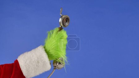 Photo for The Grinchs green haired hand holds an antique telephone receiver on a blue isolated background. Gift Snatcher Cosplay. Christmas and New Year celebration concept. Blue screen, chroma key - Royalty Free Image
